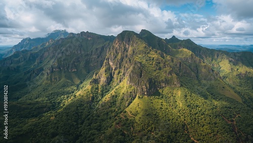 Mountains Rise Above Green Landscape With Clouds in the Sky and Sunlight Hitt...