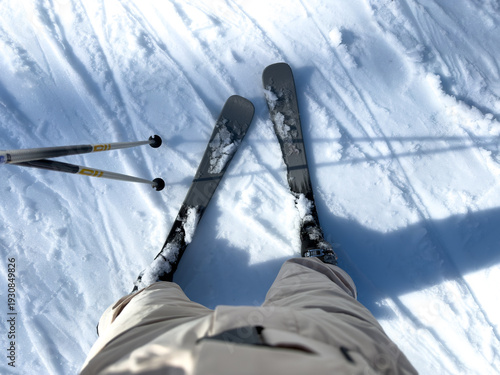 First person view skiing downhill on snowy ski slope, skis and ski poles in frame, winter sports activity at alpine mountain resort