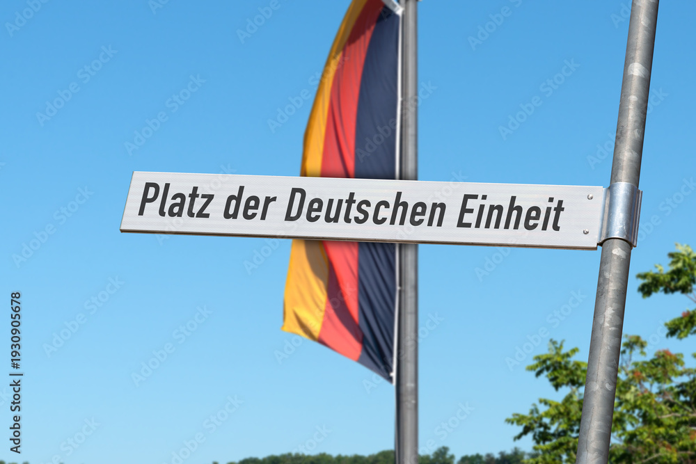 Fototapeta premium Straßenschild „Platz der Deutschen Einheit“, mit der deutschen Flagge im Hintergrund, (Symbolbild)