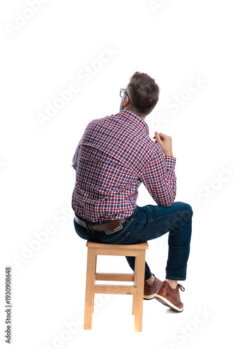 Back view of pensive casual man sitting on stool