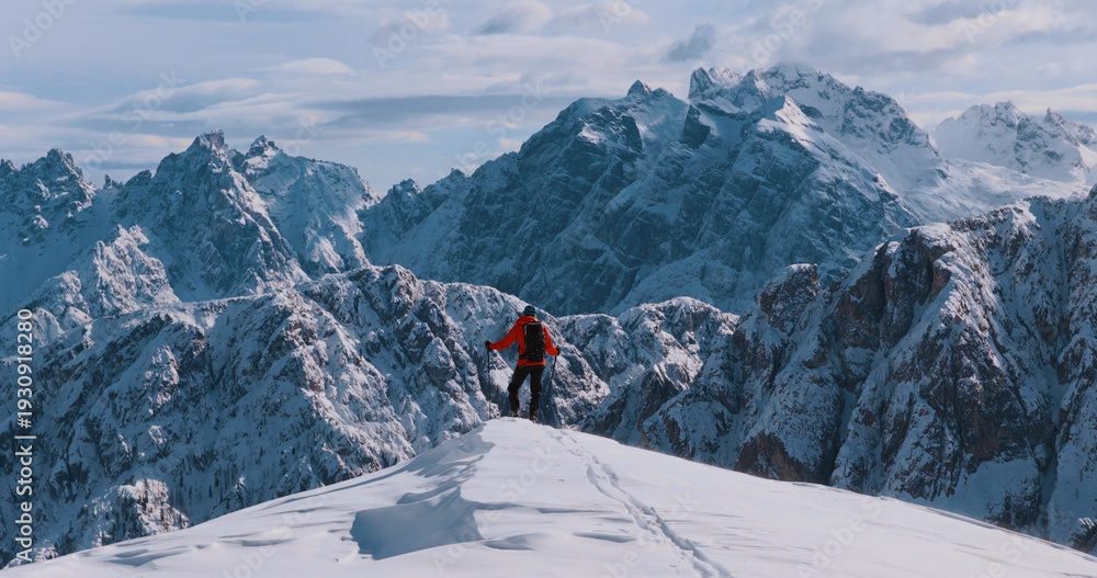 Obraz premium Ski mountaineer standing on a snowy cliff in the Dolomites with majestic alpine peaks in the background, capturing winter adventure, solitude and breathtaking mountain scenery.