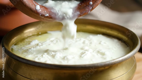 Creamy White Yogurt Being Poured From a Traditional Clay Pot Into a Vintage Brass Bowl With Soft Natural Lighting Creating a Healthy Dairy Food Preparation Scene