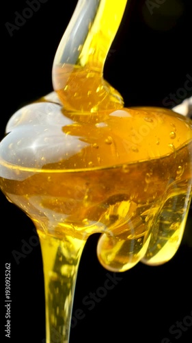 Natural bee honey flowing into a spoon and dripping from it, macro on a black background.