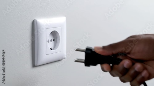 Wallpaper Mural Person's hand plugging black power cable into white wall socket Torontodigital.ca