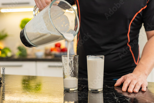 Bild auf Leinwand Man pours protein smoothie from blender into glass on kitchen counter for healthy nutrition