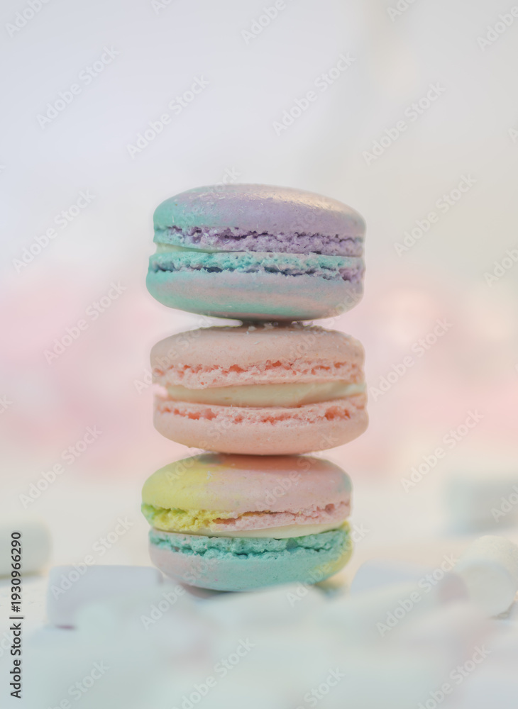 Fototapeta premium Stack of colorful macarons in pastel shades on light background. French almond cookies with creamy filling. Minimal dessert composition with soft tones and copy space.