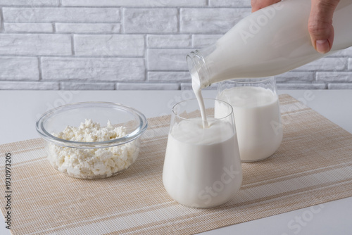Pouring homemade kefir, buttermilk or yogurt with probiotics. Yogurt flowing from glass bottle on light background. Probiotic cold fermented dairy drink. Trendy food and drink