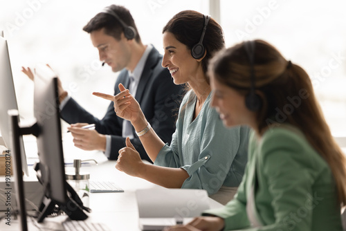 Foto Diverse customer care team sitting at desk in headsets communicating online via