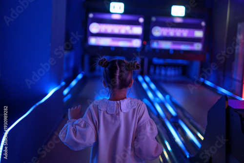 The girl is happy to play bowling and score a strike. The dark neon game room of the entertainment center