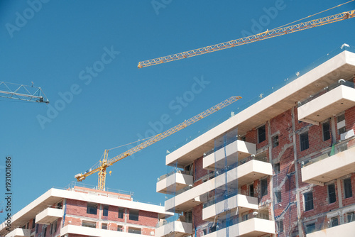Construction site with partially built modern residential buildings and cranes under clear blue sky