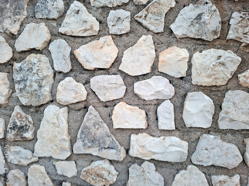 Rustic Mediterranean stone wall with uneven natural rocks set in grey mortar for architectural backgrounds and designs