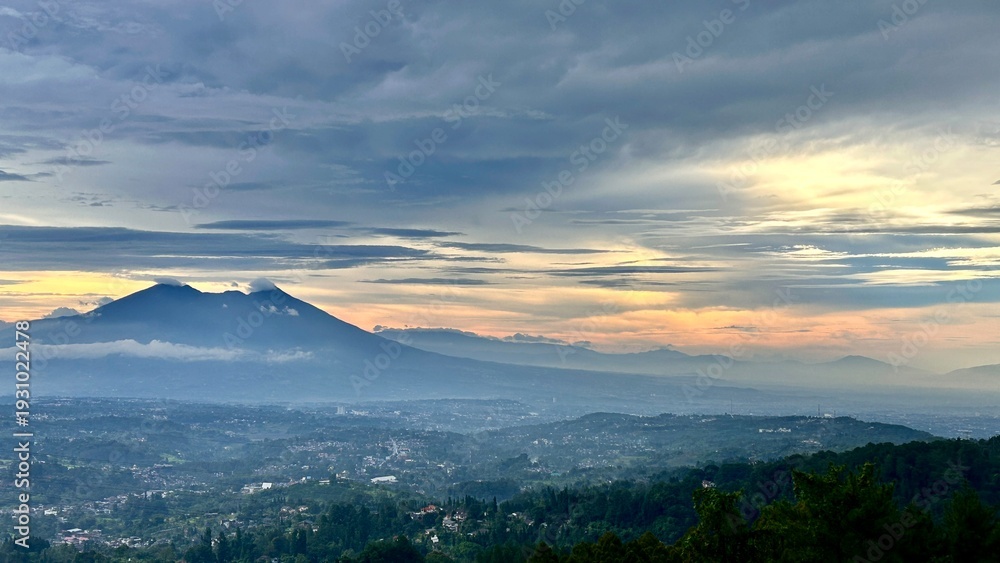 Fototapeta premium Scenic view of a vibrant sunset over a distant mountain range, featuring dramatic sky colors transitioning from deep blue to bright orange and golden yellow.