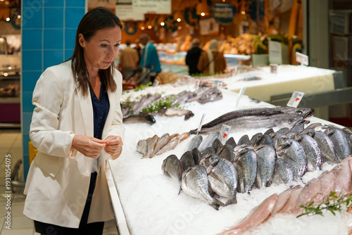 Middle-aged woman choosing fresh fish and seafood on ice at a supermarket counter in Spain, Mediterranean diet and everyday grocery shopping concept