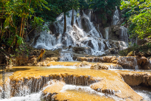 Serene tropical Dai Chong Thong waterfall cascade over limestone rock in lush forest at Sangkhlaburi, Kanchanaburi, Thailand under soft morning light