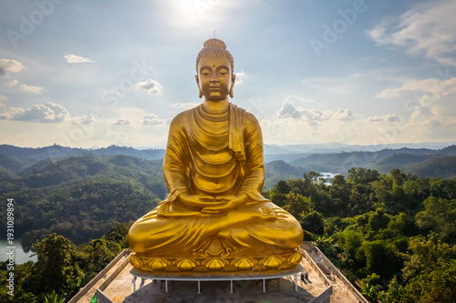 Breathtaking aerial panorama of the large golden Phra Phuttha Lokanat Satsada meditation Buddha statue at Wat Wang Wiwekaram overlooking winding river, lush forest, and layered mountain landscape in S