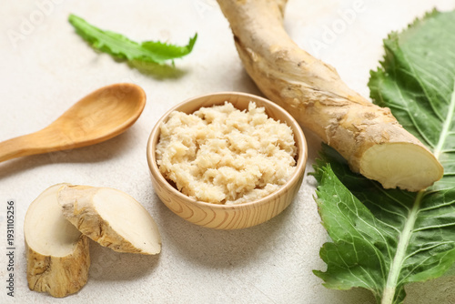 Photos Bowl of horseradish sauce with root, slices, leaf and spoon on light background