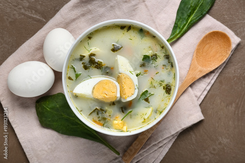 Obraz na płótnie Bowl of tasty green borscht with eggs, spinach leaves and wooden spoon on brown