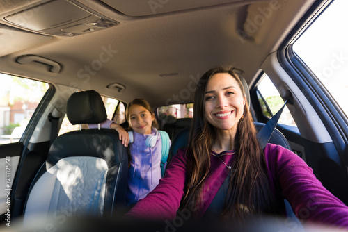 фотографія Mother driving car with daughter in backseat, both smiling, traveling to school