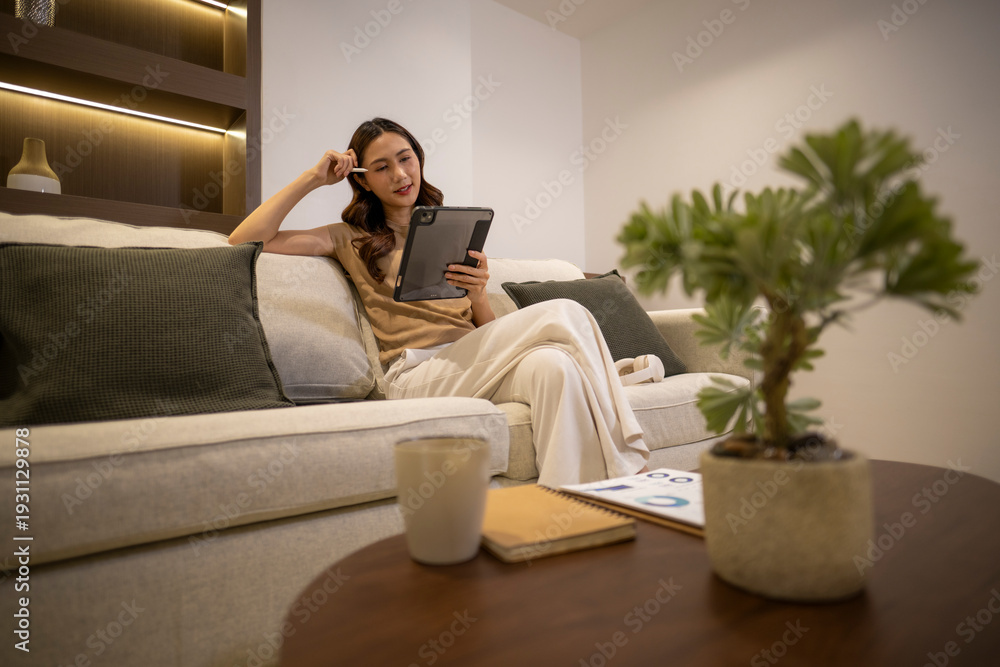 Obraz premium Asian woman working remotely on tablet at home