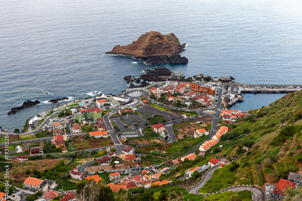 Fototapeta premium Porto Moniz coastal village on Madeira Island, Portugal. Red-roofed buildings near Atlantic Ocean. Rocky shoreline with volcanic cliffs. Scenic view of natural seascape.