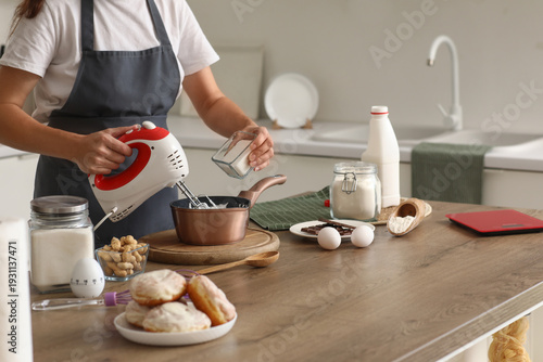 Woman whipping egg albumen with mixer at table in kitchen