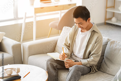 Young Asian man writing som...