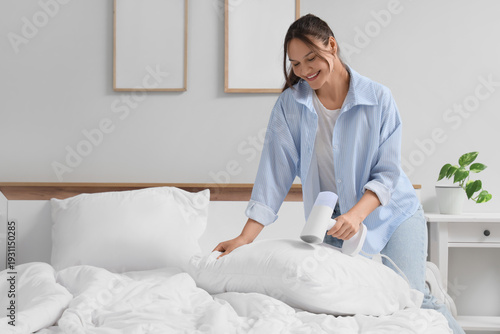 Tableau sur toile Beautiful young woman steaming pillow with modern garment steamer at home, close