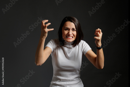 Angry young woman gritting teeth and raising clenched hands in a gesture of fury and aggression.