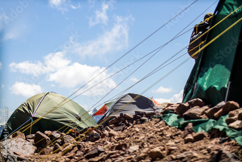 Φωτογραφία Mountain base camp with several colorful expedition tents pitched on rocky terrain under a blue sky with clouds