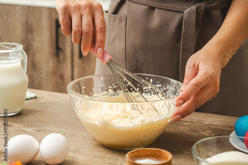 Wallpaper Mural A woman is mixing ingredients in a bowl with a whisk. The bowl is filled with a white mixture, and there are eggs and a cup nearby. The woman is wearing an apron Torontodigital.ca