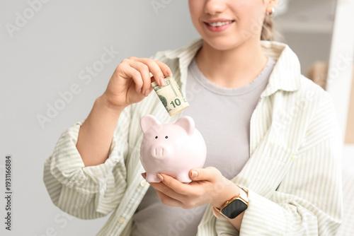 Young woman putting money into piggy bank at home, closeup