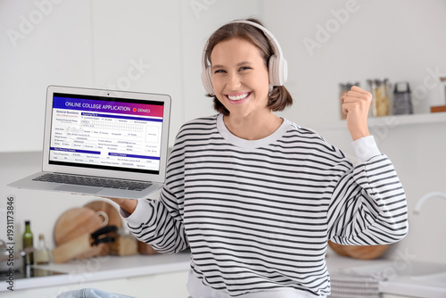 Teenage girl with headphones and college application form on laptop in kitchen