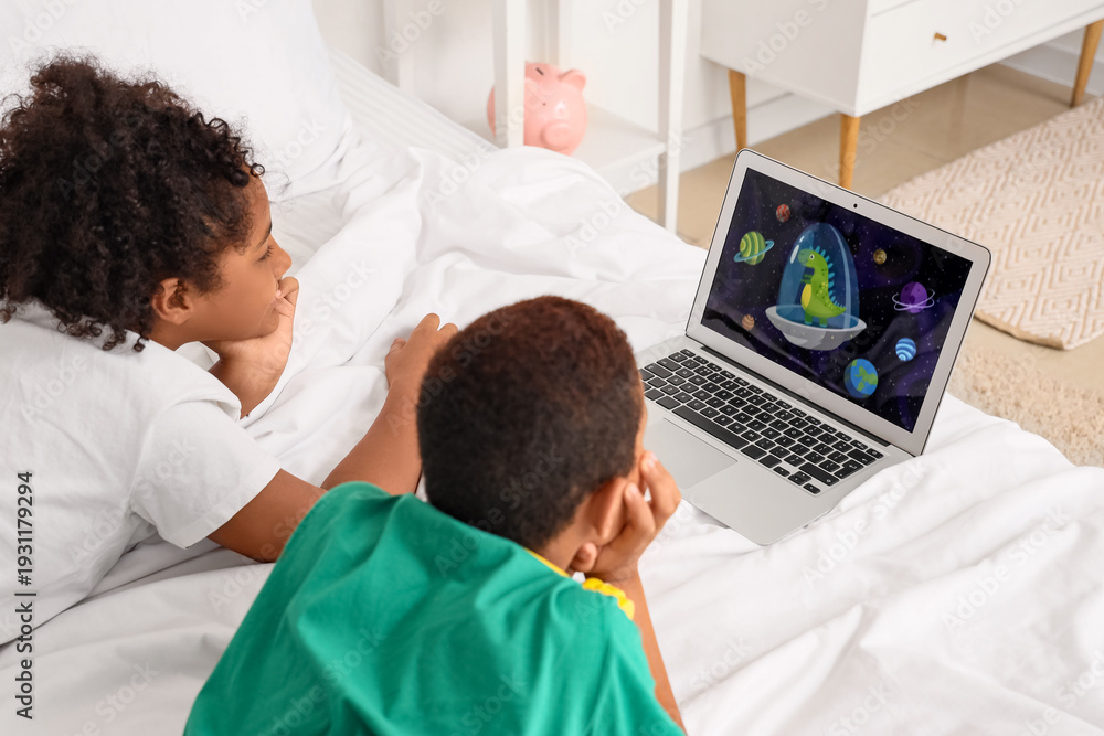 Fototapeta premium Cute African-American children watching cartoons on laptop in bedroom at home