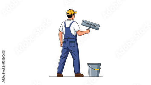 Male construction worker in blue overalls and a yellow cap stands with his back turned while holding a tool.