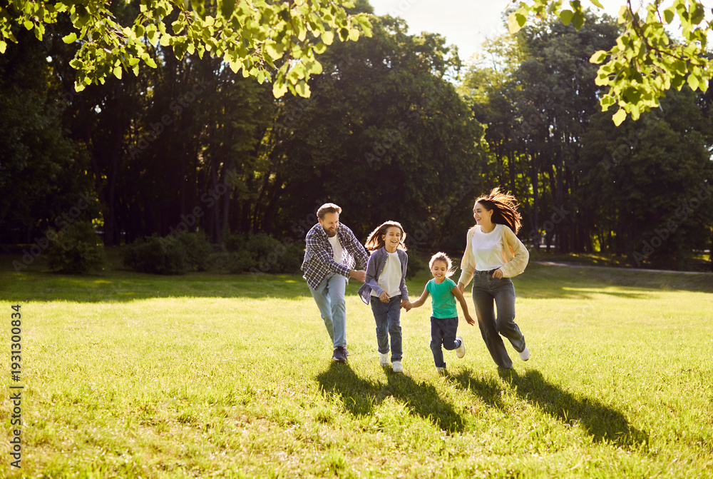 Fototapeta premium Happy friendly family enjoy running together, moving in green field, park feeling connection and enjoying peaceful day, warm sunny light, summer fun weekend to enjoy beautiful nature day out