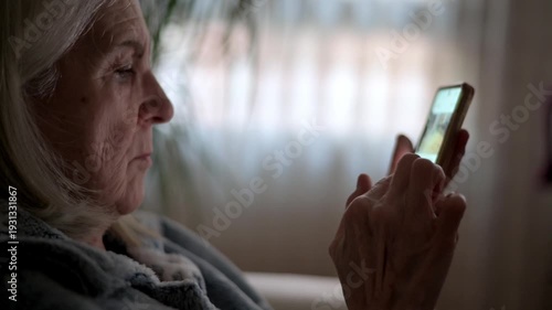 Older Woman Focused On Her Smartphone In A Cozy Home Setting With Soft Lighting