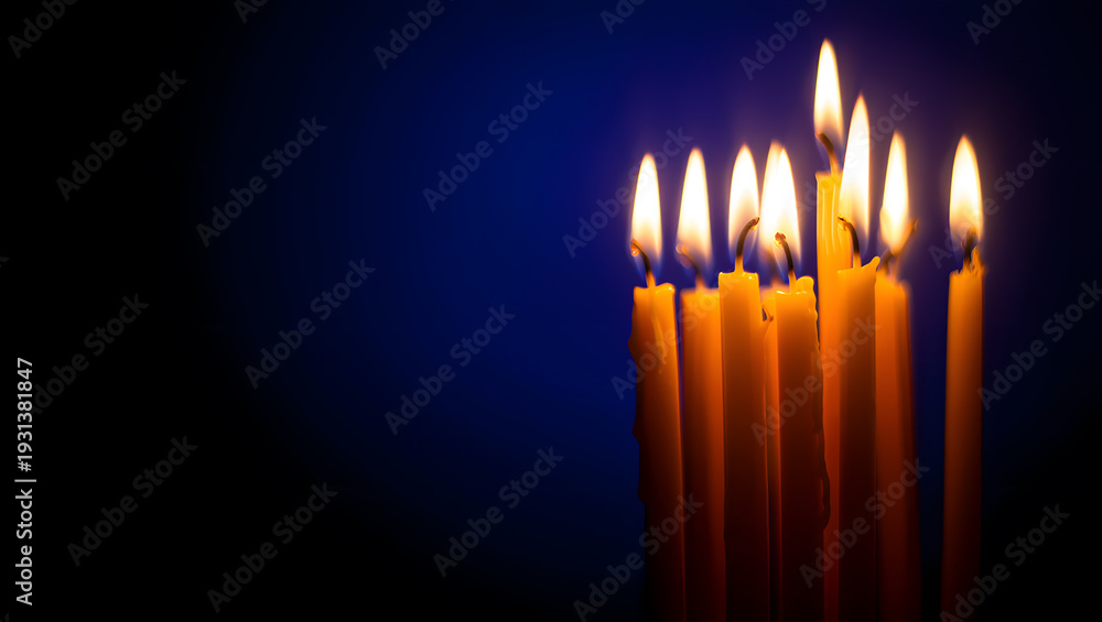 Fototapeta premium A cluster of tall yellow candles burning brightly against a dark blue background.