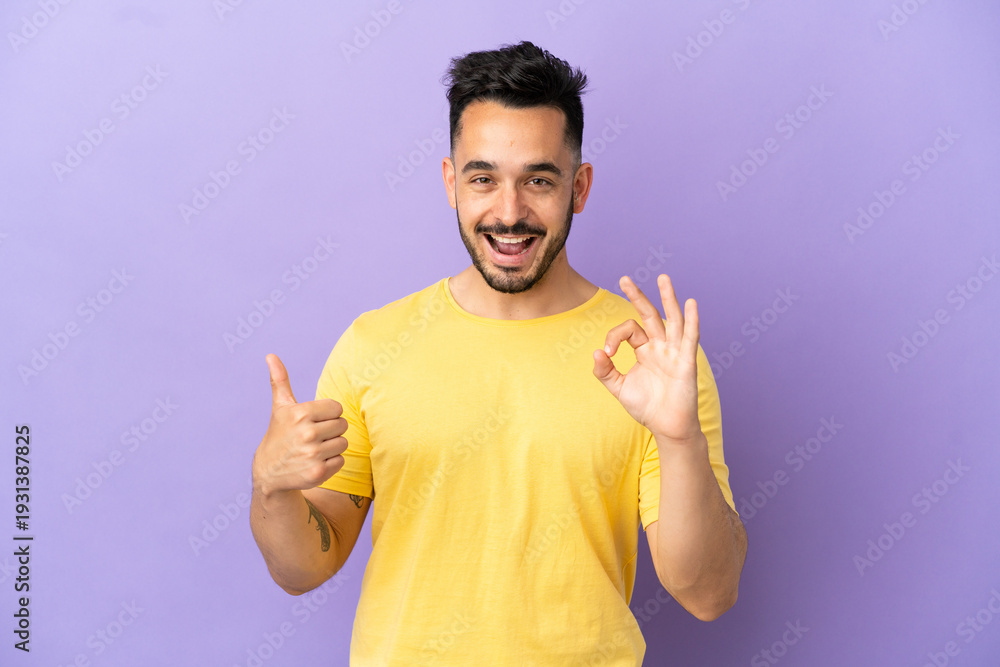 Fototapeta premium Young caucasian man isolated on purple background showing ok sign and thumb up gesture