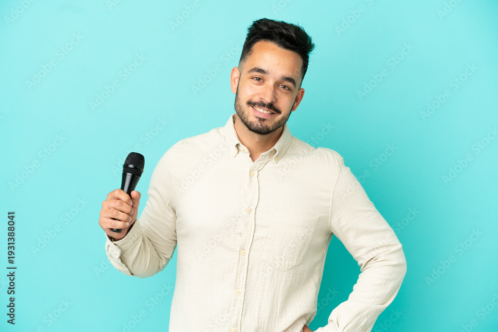 Naklejka premium Young caucasian singer man isolated on blue background posing with arms at hip and smiling