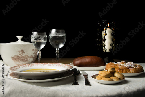 Mesa con sopa, embutido, galletas y dulce iluminada por vela.