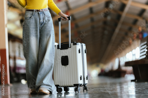 Stylish young woman traveling at train station with suitcase, traveling alone on vacation or business trip, enjoying summer city adventure.	