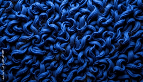 A blue rug with wavy patterns, placed against a grey background. The rug has a textured appearance, suggesting a plush feel, and its color contrasts sharply with the subdued tones of the backdrop.