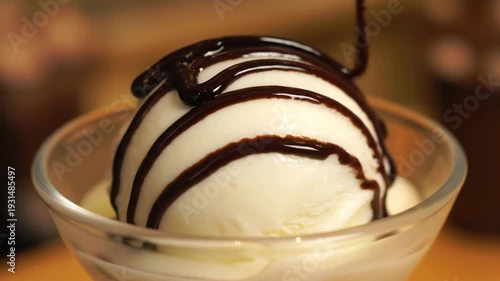 Delicious vanilla ice cream with chocolate syrup being poured on top in a glass bowl.