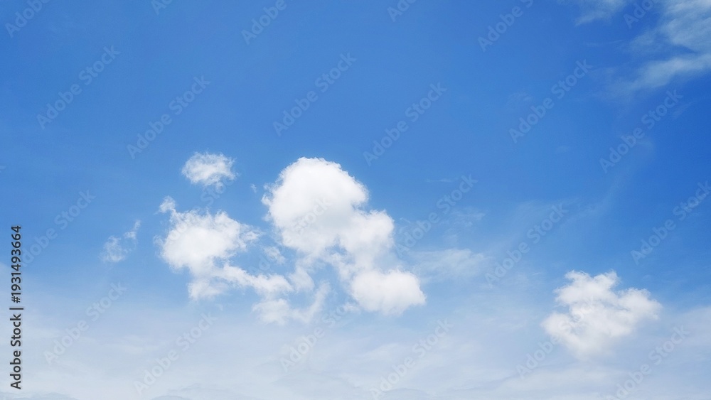 Fototapeta premium Beautiful white clouds floating in a clear blue sky. Natural daylight sky background with soft clouds. Blue sky texture with a calm and clean pattern.