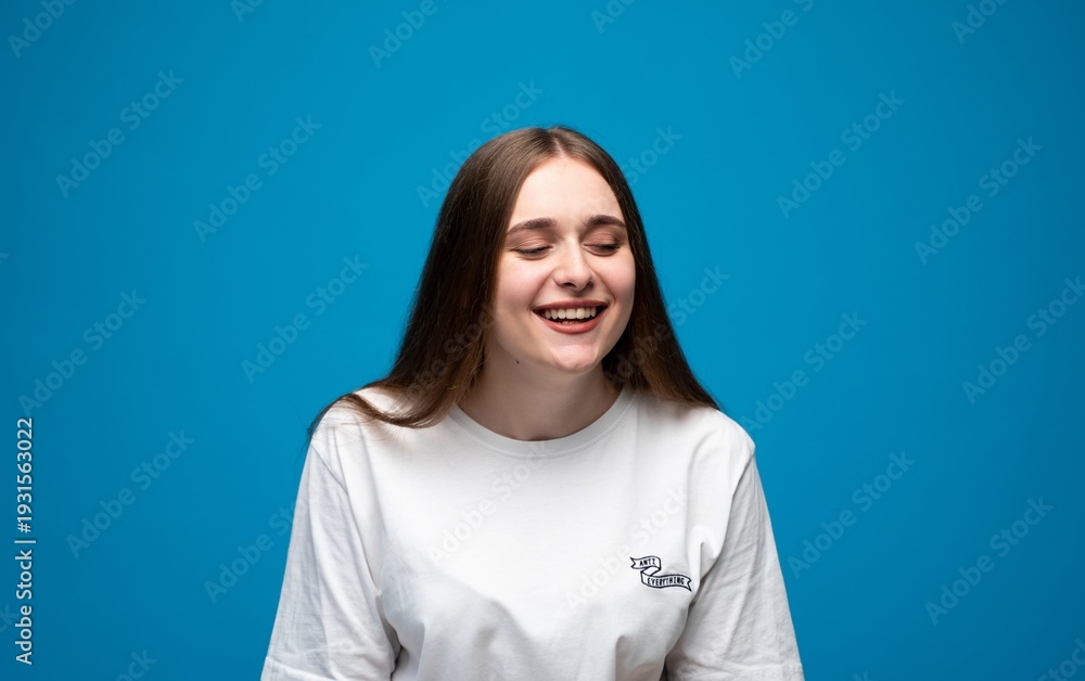 Obraz premium Young woman with closed eyes laughing, expressing joy, happiness, and cheerfulness on a blue background