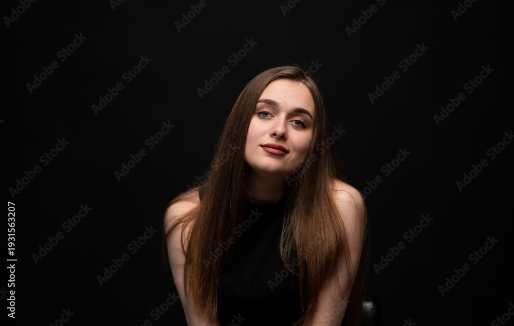 Fototapeta premium Young woman with long brown hair posing confidently in a studio portrait with a dark background