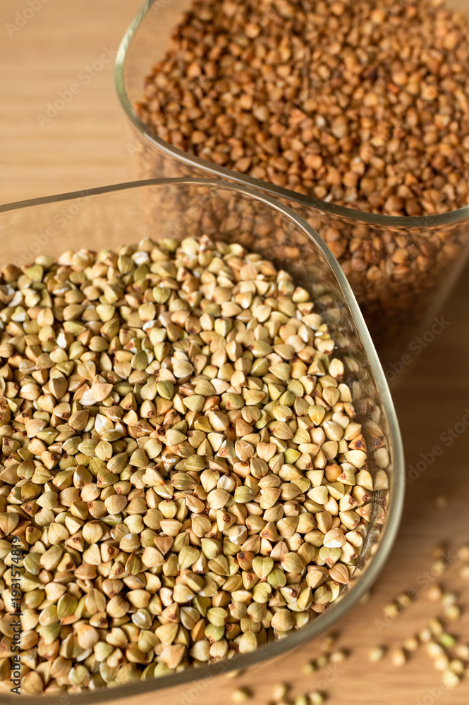 Obraz premium Green and brown buckwheat in glass jars on kitchen table top view. Close-up of gluten-free grains, healthy food and diet concept. Organic buckwheat for cooking, superfood