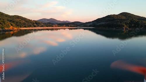 Scenic view of tranquil lake reflecting mountains and sky at sunset, showcasing serene natural beauty with calm water and lush greenery along the shoreline
