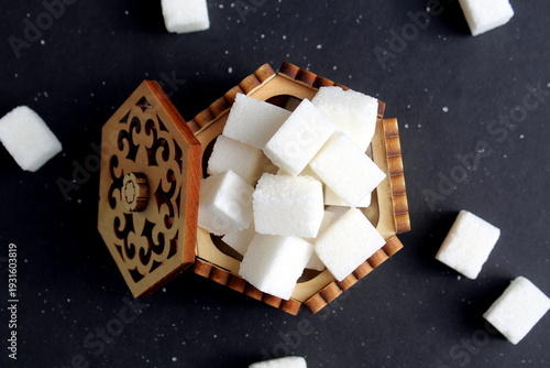 Foto On a black background there is a wooden sugar bowl with lump sugar
