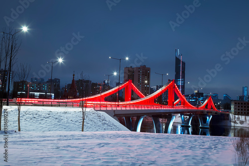 New red bridge across the Moskva River connecting the Mnyovnikovskaya and Filevskaya floodplains illuminated in the night, Moscow, Russia